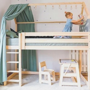 May include: A wooden loft bed with a light green canopy and a small desk and chair underneath. The bed has a ladder for access and is decorated with string lights. A child is reaching for a book on the bed.