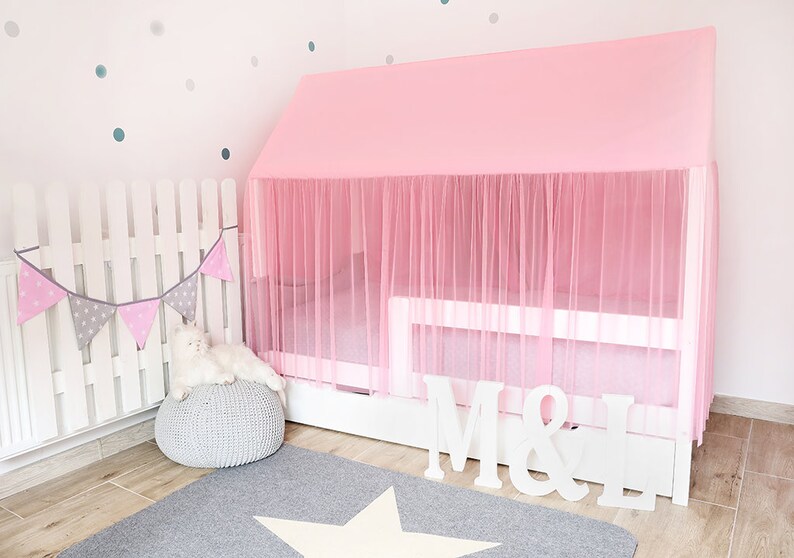 Puede incluir: Una cama con dosel rosa con un marco blanco y un caj&oacute;n blanco con las letras "M & L" en la parte delantera. La cama est&aacute; decorada con un dosel de tul rosa y una valla blanca con una pancarta gris y rosa.