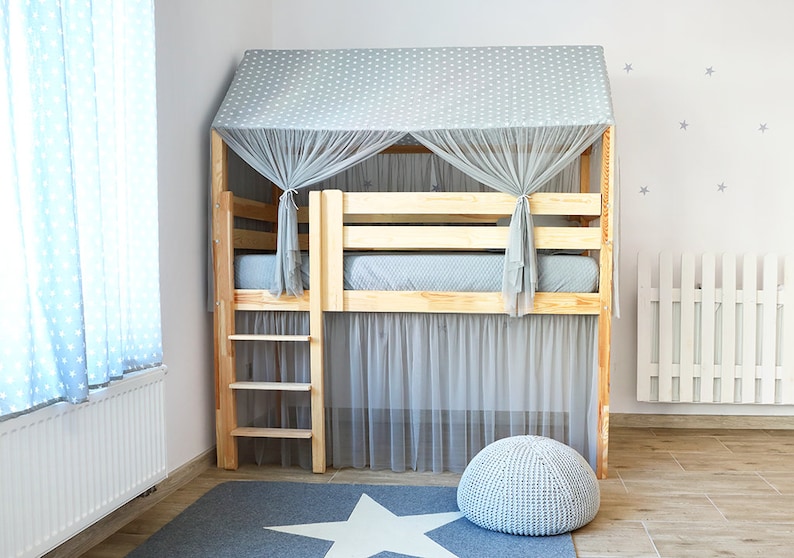 May include: A wooden bed frame with a gray and white patterned canopy and a gray mesh curtain. The bed has a ladder and a gray footstool. The bed is in a room with a white radiator and a white picket fence.