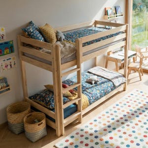 Può includere: Un letto a castello in legno chiaro con una scala integrata sul lato. Entrambi i letti sono dotati di biancheria con motivi blu e gialli, inclusi cuscini decorativi e una coperta di colore chiaro sul letto inferiore.