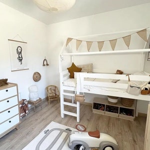 Op de afbeelding: Lichte kinderkamer met een wit hoogslaper, een speelgoedauto en een weg-speelmat. De kamer is ingericht in neutrale tinten, waaronder een beige stervormig kussen en een geweven slinger.