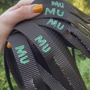 May include: Close-up of black webbing straps with the word "MU" printed in green on each strap.