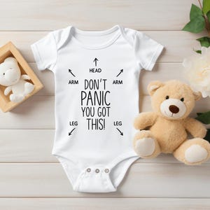 Pode incluir: Um macacão branco para bebê com texto preto que diz "Não entre em pânico, você consegue!" com setas apontando para a cabeça, os braços e as pernas.