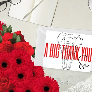 May include: A white thank you card with a black elephant illustration and red text that reads "A BIG THANK YOU Soror". The card is on a white envelope, with a bouquet of red flowers and a notebook in the background.