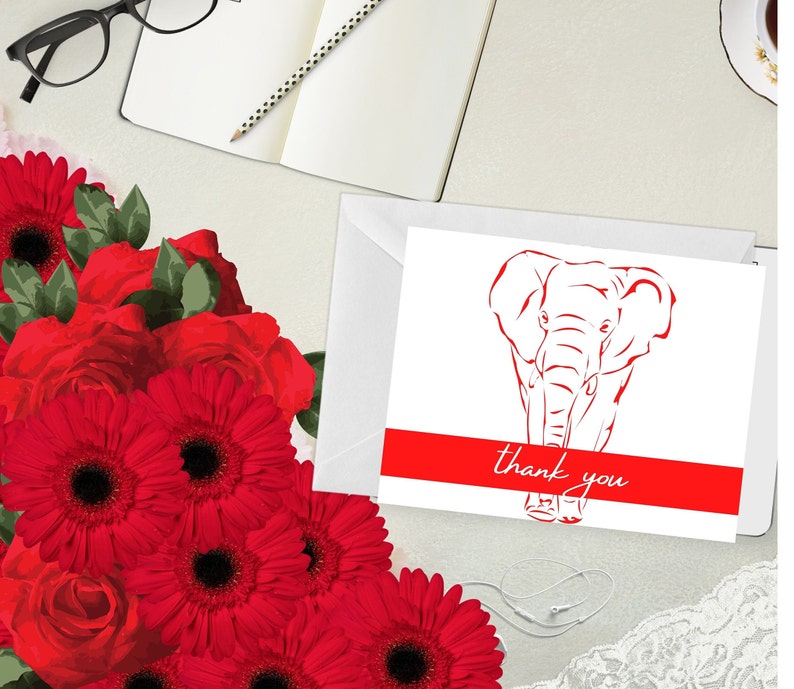 May include: A white greeting card featuring a red elephant illustration and the words "thank you". The card is in a white envelope. Red flowers and a notebook with a pencil are in the background.