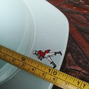 May include: A light blue ceramic ashtray with a red and white walking man logo. The ashtray is 6 inches in diameter.