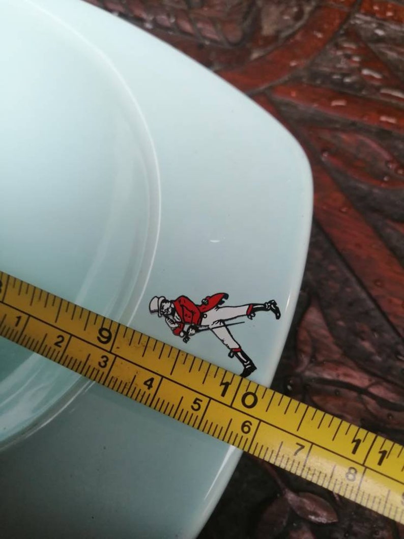 May include: A light blue ceramic ashtray with a red and white walking man logo. The ashtray is 6 inches in diameter.