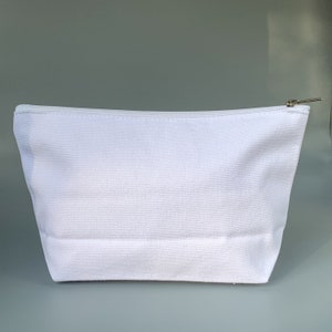 May include: A white canvas zippered pouch with a silver zipper pull. The pouch is empty and has a smooth, textured surface.