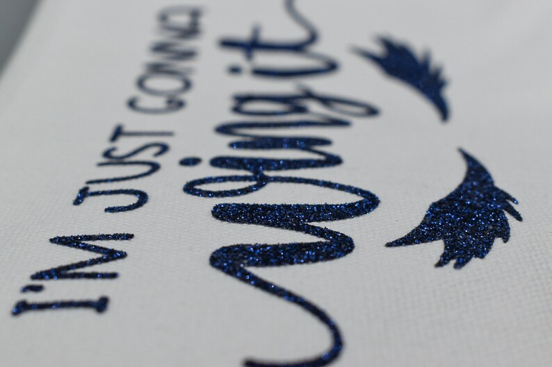 May include: A white canvas tote bag with the text "I'm just gonna wing it" in blue glitter lettering. The text is in a cursive font and there are two blue glitter wings on either side of the text.