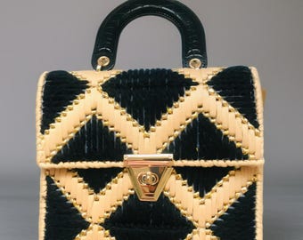 May include: A structured handbag with a geometric pattern. The bag features a black and beige woven design with gold-colored accents. It has a dark green handle and a gold-colored clasp. The bag is a small, square shape.