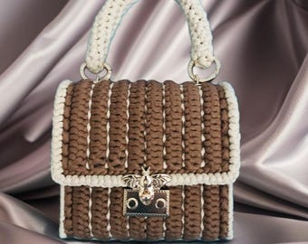 May include: A brown and white crocheted handbag with a top handle and a silver bee clasp. The bag has a rectangular shape with a flap closure and a white crocheted handle. The background is a satin fabric.