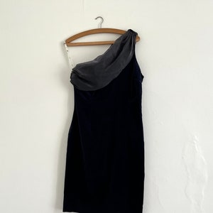 Puede incluir: Un vestido negro de terciopelo de una sola manga con una superposición de gasa gris en el hombro.