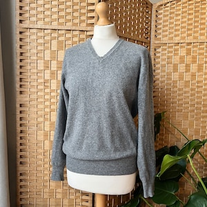 May include: A grey v-neck jumper with long sleeves. The jumper is made of a soft, comfortable material.