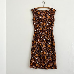 Puede incluir: Un vestido marrón sin mangas con un patrón geométrico en tonos marrones, naranjas y blancos. El vestido tiene un lazo en la cintura.
