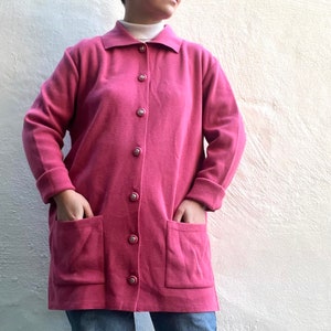 May include: A long-sleeved pink cardigan with a button-up front and two large pockets. The cardigan is made of a soft, fuzzy material.