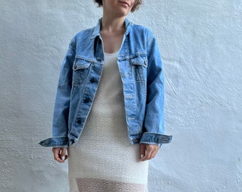 May include: A light blue denim jacket with a white knit dress underneath. The jacket has a classic design with button closures and two front pockets.