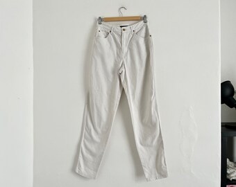 May include: White straight-leg jeans with a classic five-pocket design. The jeans are hanging on a wooden hanger.