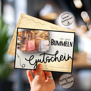 May include: A gift certificate with the words "Wir gehen Bummeln" and "Gutschein" in black script. The certificate features an illustration of shopping bags and a street scene. The certificate is held in a hand.