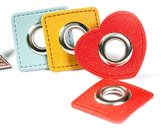 May include: Five colorful leather shapes with metal eyelets. The shapes include a star, two squares, a heart, and a diamond. The star is rose gold, the squares are light blue and yellow, the heart is red, and the diamond is red.