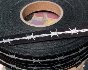 May include: A roll of black ribbon with silver glitter barbed wire design. The ribbon is wound around a cardboard core.