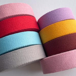 May include: A stack of colourful cotton webbing rolls in various colours including red, pink, yellow, blue, grey, and brown.