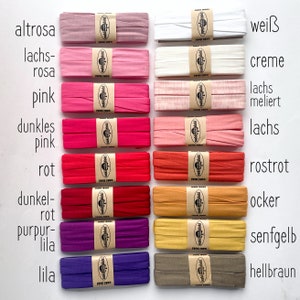 May include: A collection of eighteen folded fabric strips arranged in two columns, each secured with a tan paper band featuring the text oaki doki. The strips display a spectrum of colors including white, cream, pink, red, purple, yellow, and brown.