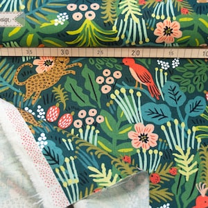 May include: A dark green fabric featuring a repeating pattern of orange leopards, red birds, pink flowers, and various green foliage. A wooden ruler is placed across the top, showing measurements from 5 to 40 centimeters. The fabric has a white reverse side.