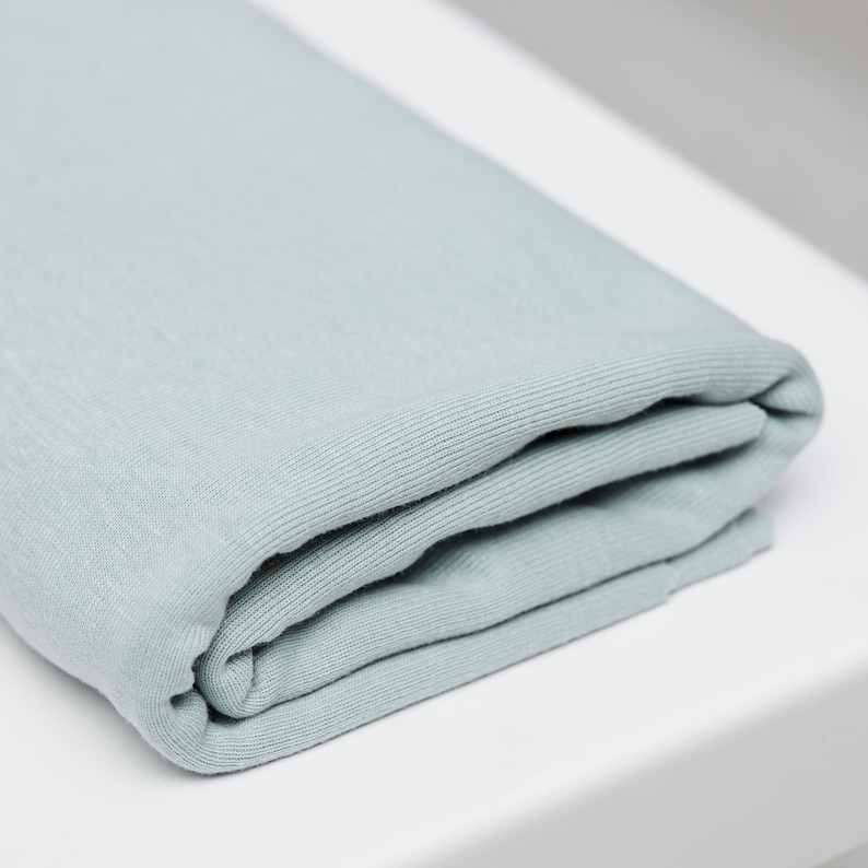 Puede incluir: Tela azul claro doblada, posiblemente una manta o textil, con una textura acanalada. La tela est&aacute; cuidadosamente doblada, mostrando la suavidad del material y su potencial de confort. El color es un azul pastel apagado.