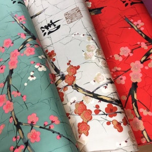 May include: Three fabric swatches featuring a Japanese-inspired floral design. The fabric on the left is a light teal colour, the middle fabric is a light beige colour, and the fabric on the right is a bright red colour. All three fabrics feature a delicate floral pattern with pink and white blossoms and black branches.