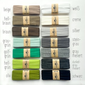 May include: Fourteen folded fabric strips arranged in two columns, each secured with a tan paper band labeled oaki doki. Colors include beige, light brown, brown, sage green, emerald, lime, olive, white, cream, silver, charcoal, heather gray, dark heather gray, and black.