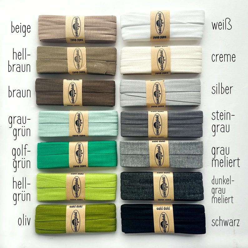 May include: Fourteen folded fabric strips arranged in two columns, each secured with a tan paper band labeled oaki doki. Colors include beige, light brown, brown, sage green, emerald, lime, olive, white, cream, silver, charcoal, heather gray, dark heather gray, and black.
