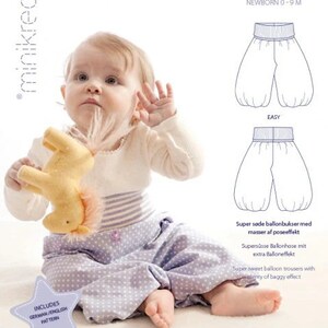 May include: A baby wearing a white long-sleeved shirt and lavender polka-dot pants. The baby is holding a yellow stuffed animal. The image includes text that says "BALLONBUKS 10301" and "NEWBORN 0-9 M".