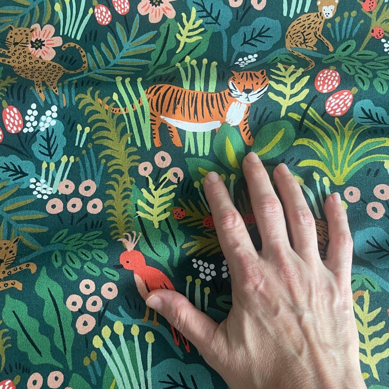 May include: A dark green fabric featuring a repeating pattern of orange tigers, spotted leopards, and red birds nestled among various green jungle plants, ferns, and small pink and white berries. The textile has a dense, colorful botanical print.