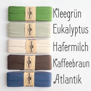 May include: Five folded fabric strips in clover green, eucalyptus, oat milk, coffee brown, and atlantic blue. Each strip is secured with a tan paper band featuring the text oaki doki and a tree logo. The corresponding color names are printed in black text.