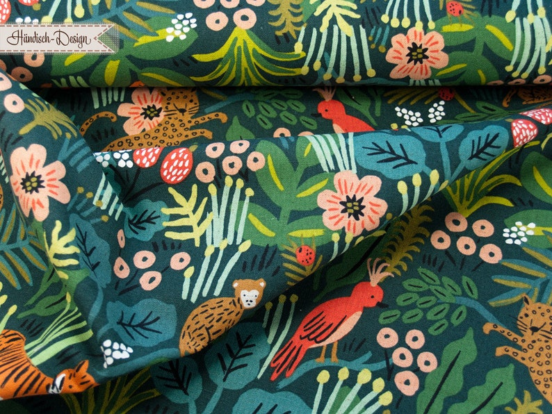 May include: A dark green fabric featuring a repeating pattern of orange birds, spotted leopards, and monkeys amidst pink flowers, berries, and various green leaves. A small rectangular label in the top left corner displays the text H&uuml;ndisch-Design.