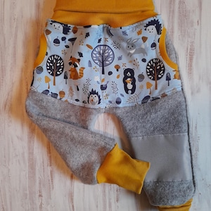 Könnte beinhalten: Graue Babyhose mit blau-gelbem Bund und Bündchen. Der Bund zeigt eine Waldszene mit Waschbär, Bär, Igel und Kaninchen. Die Bündchen und der Bund sind leuchtend gelb.