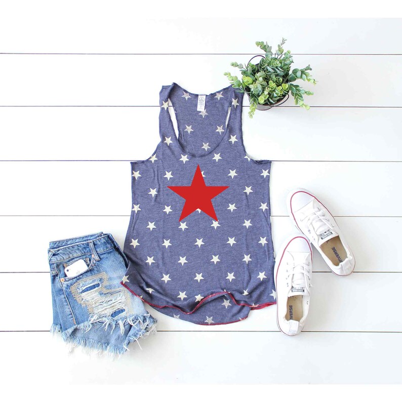 Puede incluir: Un top azul de tirantes con un patr&oacute;n de estrellas blancas y una gran estrella roja en el centro. El top est&aacute; sobre una superficie de madera blanca con un par de zapatillas blancas y una planta en maceta.