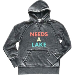 May include: A gray hooded sweatshirt with a distressed look. The text "NEEDS A LAKE" is printed on the front in colorful letters.