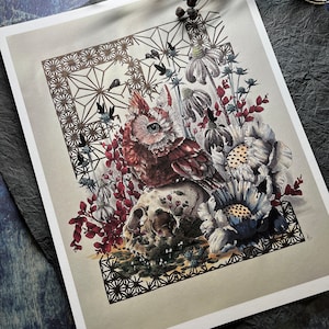 May include: A red and white owl perched on a skull surrounded by flowers and leaves. The owl has a large, yellow eye and a detailed, intricate design. The background is a geometric pattern in gold and black.