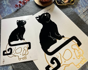 May include: Two black and white prints of a black cat sitting on a gold skull. The cat in the left print is looking up, while the cat in the right print is looking to the side. Both prints have a gold skull with a black cat tail wrapping around it.
