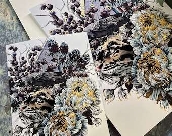 May include: Two art prints featuring a black crow, a leopard, and white flowers with gold accents. The prints are on white paper with a white background.