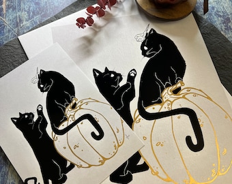 May include: Two black cats with horns on their heads are perched on top of gold pumpkins. The cats are silhouetted against a white background.