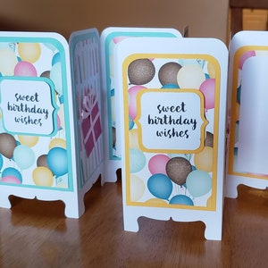 May include: A set of four folded cards with a birthday theme. Each card has a different design featuring balloons and the text "sweet birthday wishes". The cards are decorated with yellow, blue, pink, and brown colors.