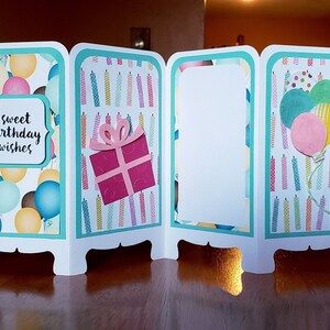 May include: A four-panel birthday card with a teal border. The front panel features a pattern of colorful balloons with the text "sweet birthday wishes". The second panel has a pattern of colorful candles. The third panel is blank. The fourth panel has a pattern of colorful candles with a cluster of balloons.