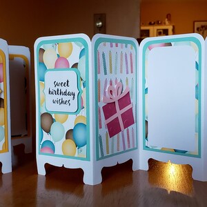 May include: A four-panel birthday card with a teal border. The panels feature different birthday-themed designs, including balloons, candles, and a gift box. The card has the text "sweet birthday wishes" on one of the panels.