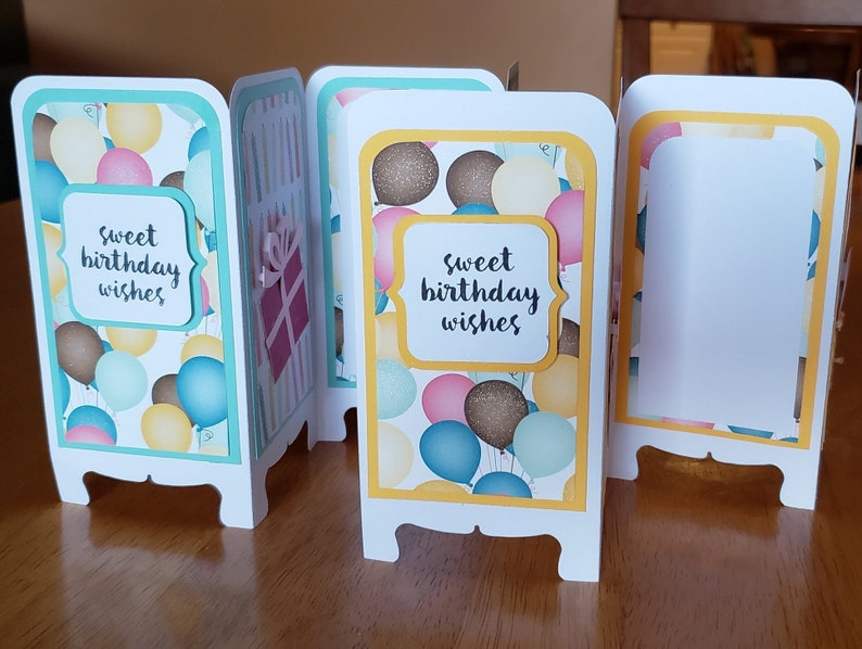 May include: A set of four folded cards with a birthday theme. Each card has a different design featuring balloons and the text "sweet birthday wishes". The cards are decorated with yellow, blue, pink, and brown colors.