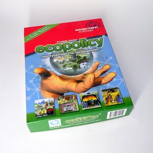 Könnte beinhalten: Ein Brettspielkarton mit dem Titel "ecopolicy" mit rotem Deckel und grünem Boden. Die Box zeigt eine Hand, die einen Globus mit einer Stadt im Inneren hält. Der Titel des Spiels ist in Grün und Blau gehalten, mit zusätzlichem Text auf Deutsch.