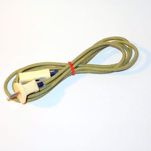 Könnte beinhalten: Ein aufgerolltes Elektrokabel mit einem cremefarbenen Stecker und einer Buchse. Das Kabel ist grün und gelb mit einem gewebten Muster und wird von einem roten Gummiband zusammengehalten. Der Stecker hat zwei Stifte.