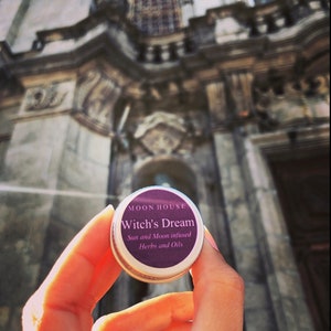 May include: A small round container with a purple label that reads "Moon House Witch's Dream Sun and Moon infused Herbs and Oils".