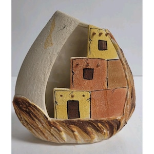 May include: A ceramic vase in the shape of a teardrop, featuring a tiered design of yellow and orange buildings with brown square windows. The vase has a textured, earthy appearance with a light beige exterior.